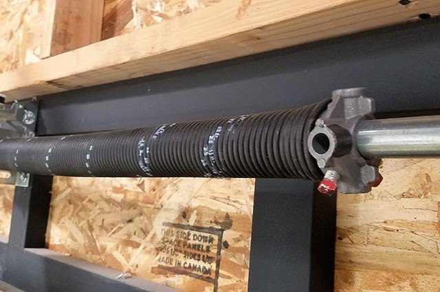 Black coiled torsion spring mounted on a steel shaft with red set screws and alignment marks.