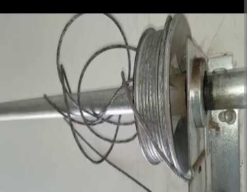 Close-up of a metal spool with tangled steel cable on a garage door shaft.