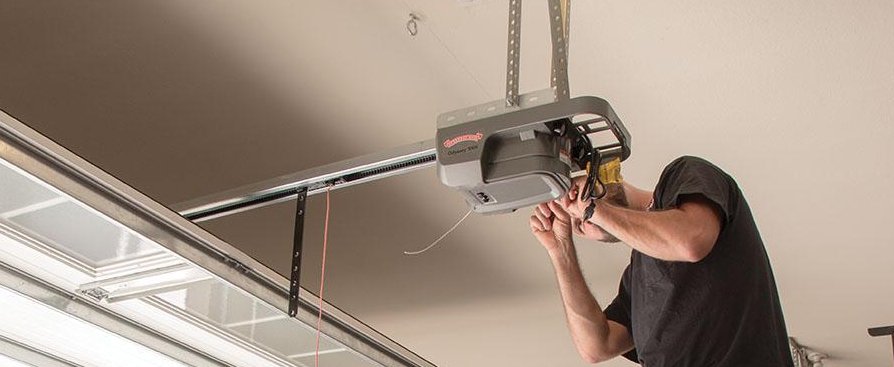 Technician adjusting a Chamberlain LiftMaster garage door opener mounted on the ceiling.